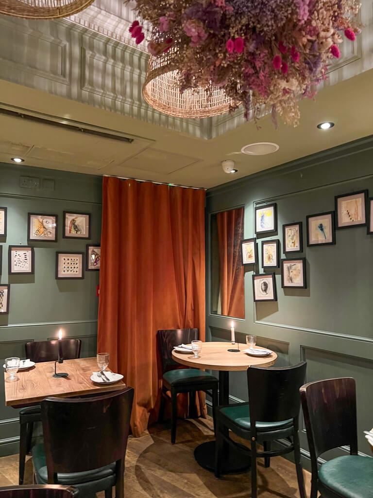 Interior of Black Lamb restaurant in Wimbledon village with drapes, dark green walls and candlelit tables. Copyright@2024 Nancy Roberts