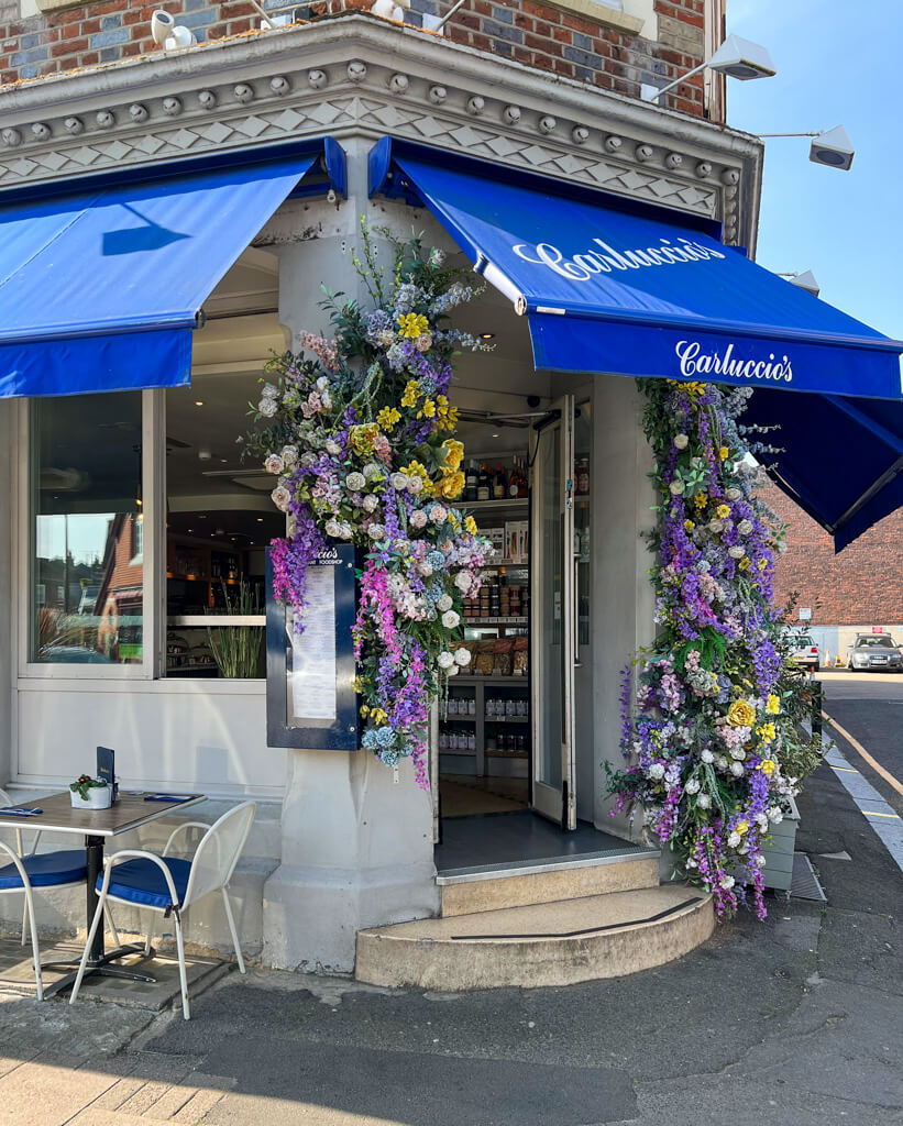 Entrance to Carluccio's Wimbledon with swags of multi-coloured flowers on either side. Copyright@2024 Nancy Roberts