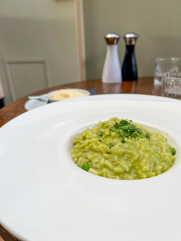 A white dish of pea and mint risotto on a white plate, for lunch at Cent Anni. Copyright@2024 Nancy Roberts