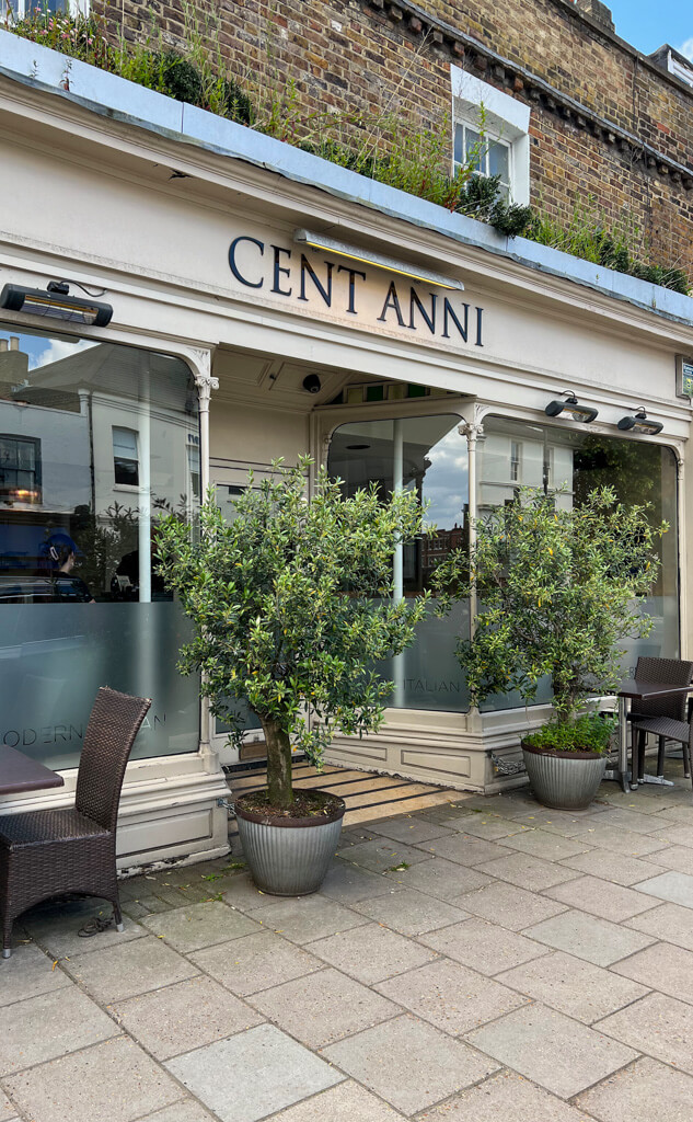 Exterior of Cent Anni Wimbledon, a period building with two large olive trees in pots flanking the entrance. Copyright@2024 Nancy Roberts