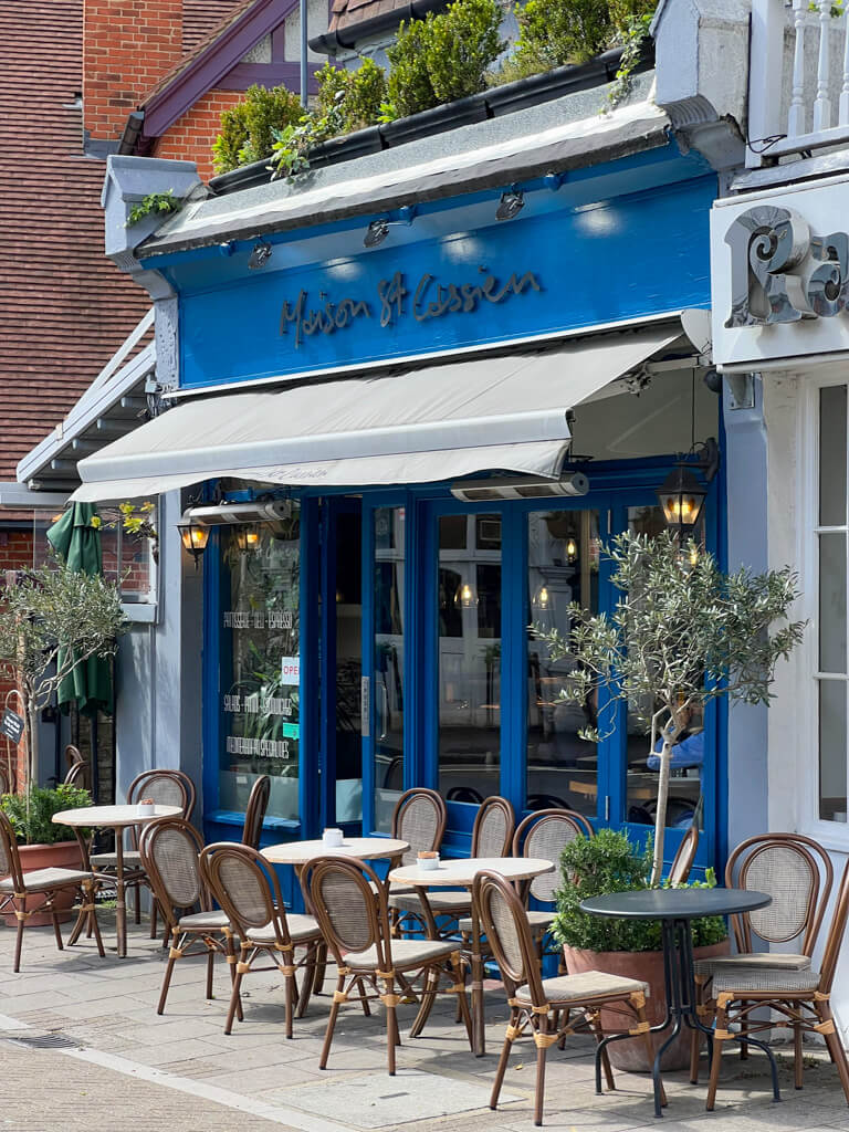 Exterior of blue-painted Maison St Cassien in Wimbledon with tables and chairs. Copyright@2024 Nancy Roberts 