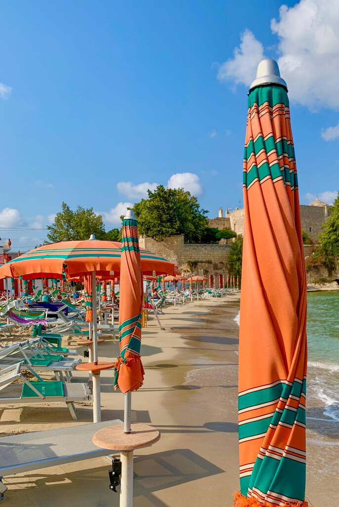 Orange and green striped parasols at the water's edge at an Italian beach club on Adriatic coast. Copyright@2024 mapandfamily.com 