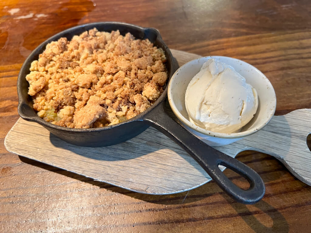 Apple crumble served in an iron dish with a side of ice cream. Copyright@2024NancyRoberts