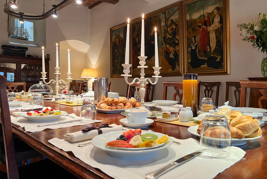 Hotel In Piazza della Signoria breakfast room with long polished antique table laid with fresh fruit and pastries and lighted candelabra. Copyright@2024 NancyRoberts 