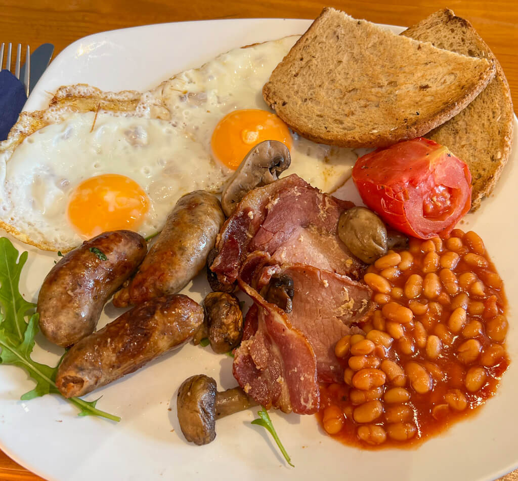 London food: a cafe-style full English with eggs, sausage, bacon, toast, beans, tomatoes and a sprig of lettuce. Copyright@2024NancyRoberts