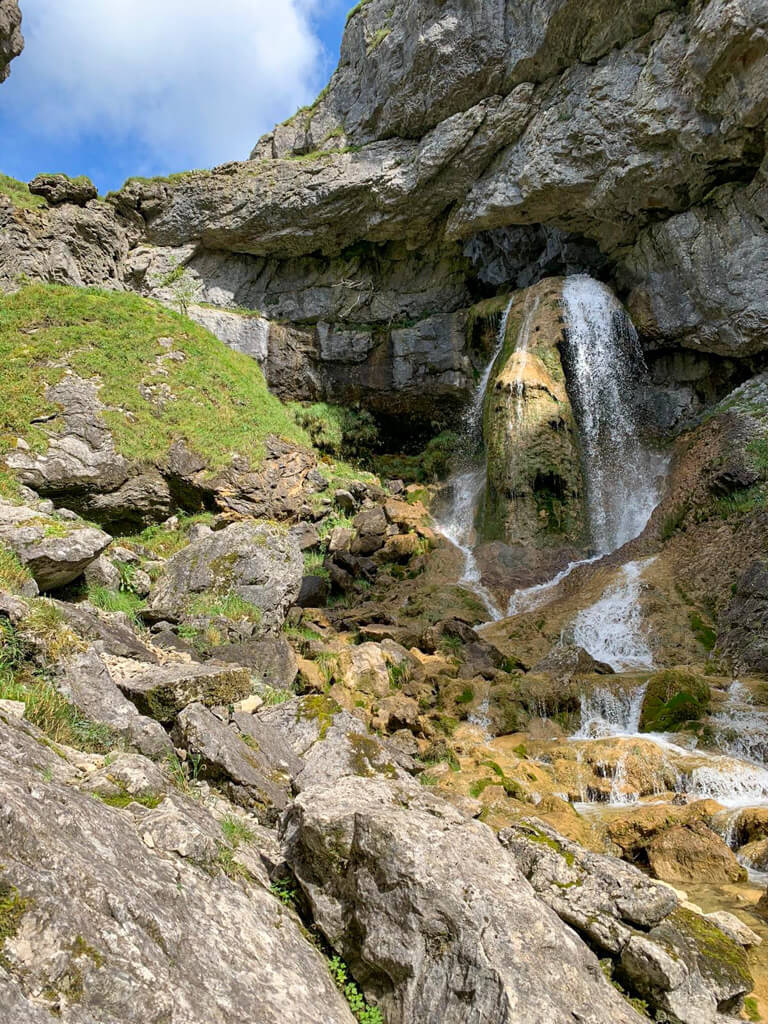 A small waterfall cascading down a craggy rock with blue sky above. Copyright@2025NancyRoberts