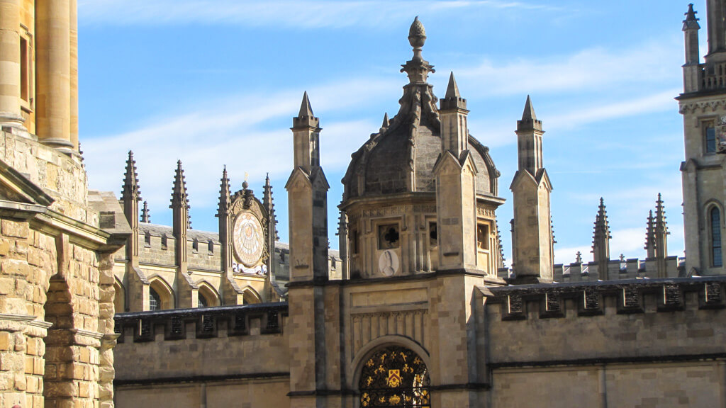 One of the most popular day trips from London England by train is to the university town of Oxford. Golden stone spires against blue sky. Copyright@2025 NancyRoberts