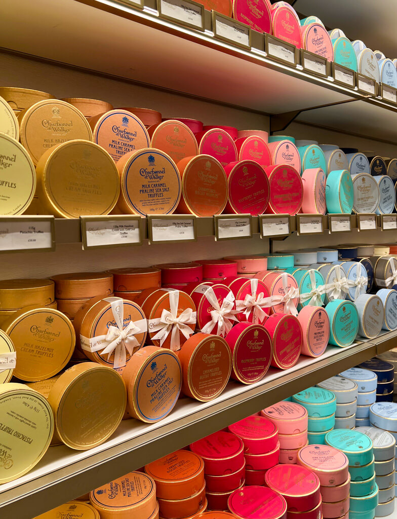 Rows of small round chocolate boxes in display shelves in graduating colours. Copyright@2025 NancyRoberts