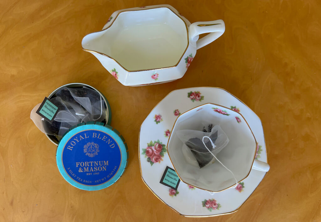 A pretty china teacup and saucer with milk jug and small tin of Fortnum&Mason teabags. Copyright@2025 NancyRoberts