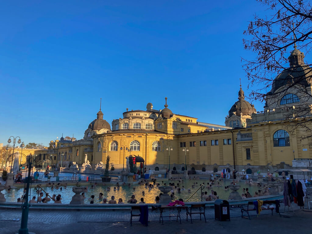 Budapest in November: historic bright ochre buildings around an outdoor thermal pool with blue sky.Copyright@2025reserved to photographer via MapandFamily