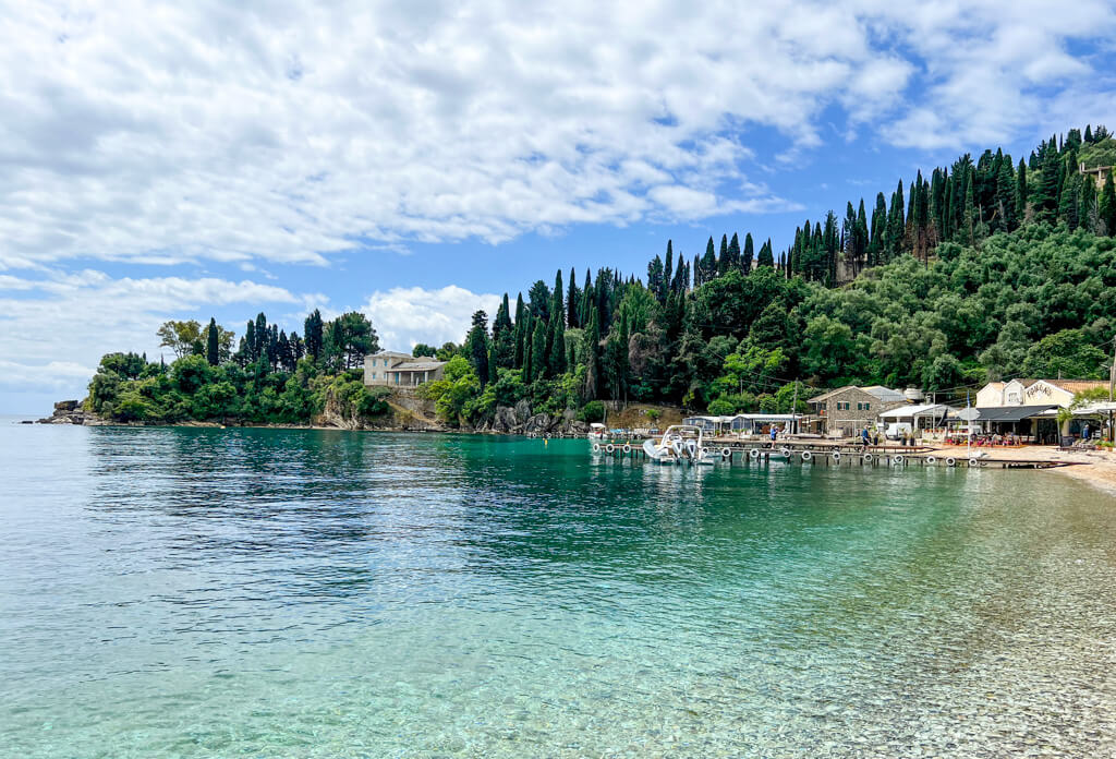 Cypresses and olive trees on the headland that shelters the clear emerald water of Agni bay near Kalami. Copyright@2025 NancyRoberts