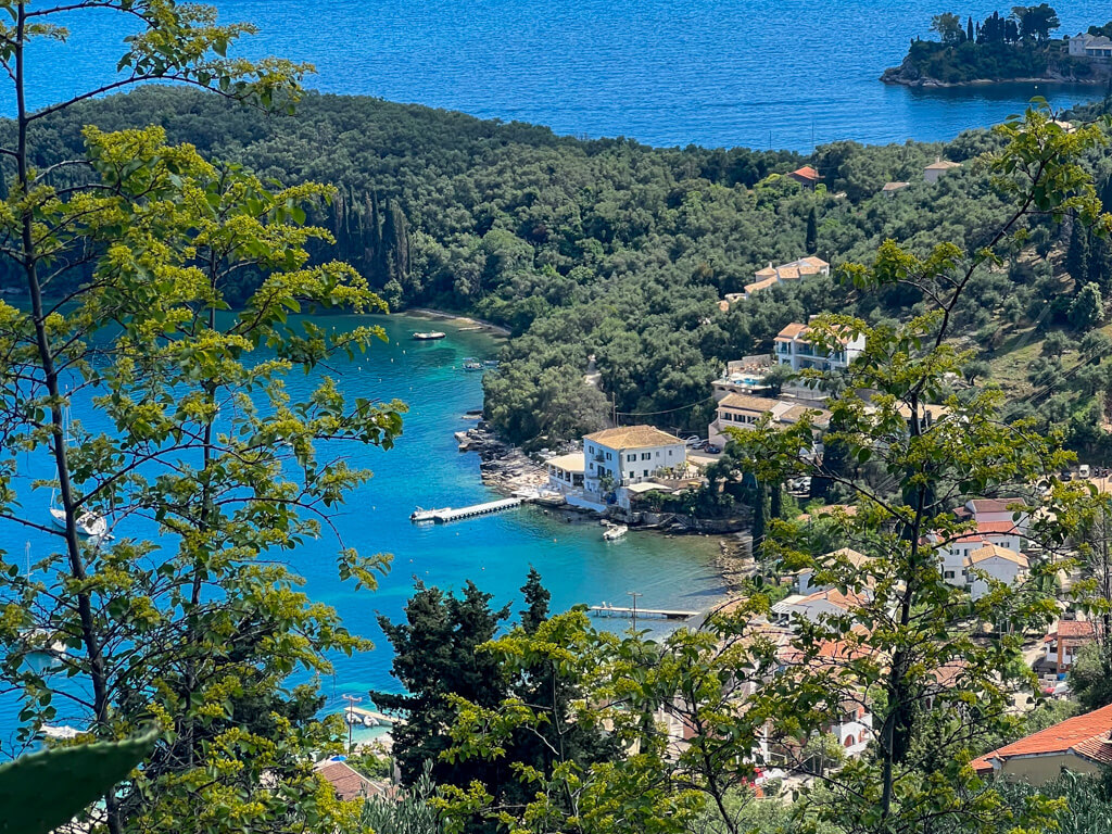 View of Kalami Corfu showing the low-built village and verdant forest around a brilliant blue bay. Copyright@2025NancyRoberts