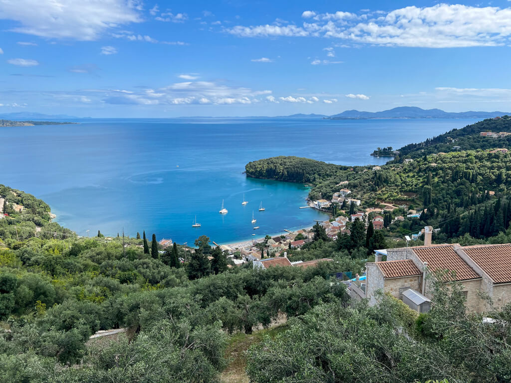 A hillside view of the village of Kalami amidst forest and olive groves with blue sea beyond. Copyright@2025 NancyRoberts