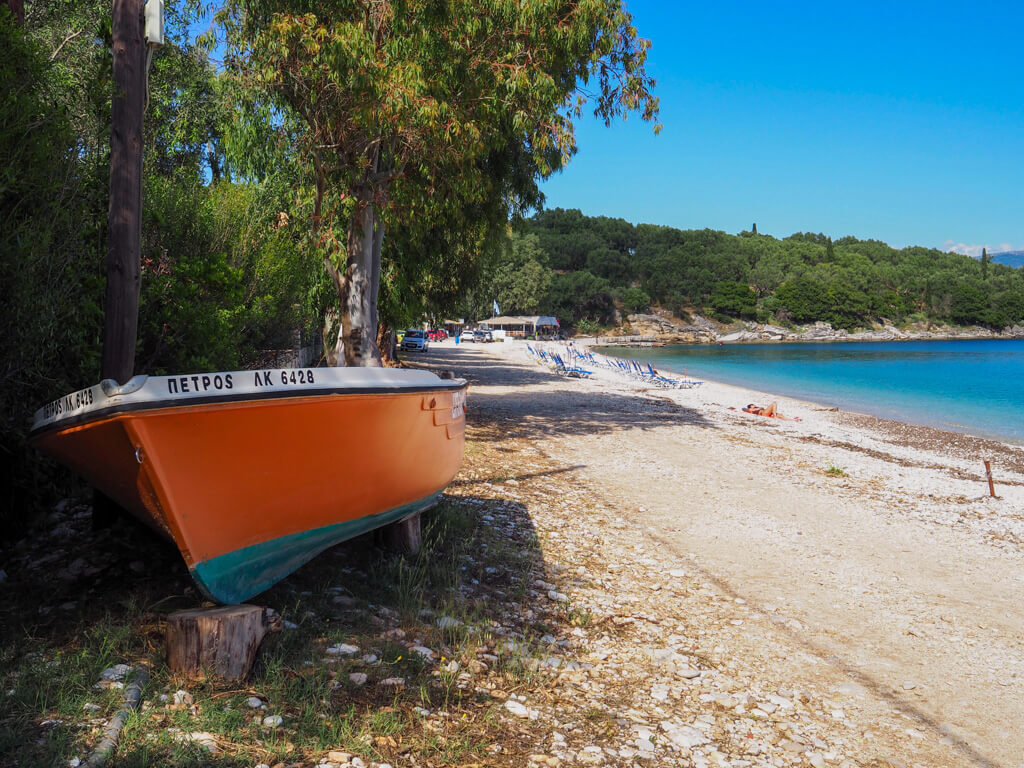 An little orange-painted boat lies in trees at the back of Kerasia beach. Copyright@2025 NancyRoberts