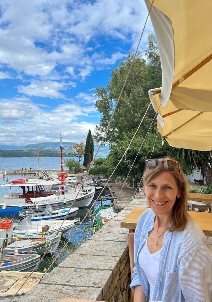Nancy, the author, sitting at the harbourside by wooden fishing boars in Kouloura. Copyright@2025 NancyRoberts