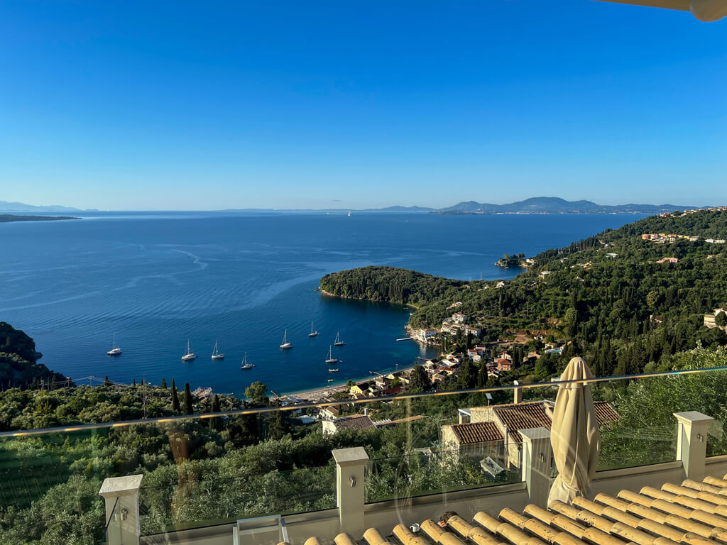 View from a terrace at Villa Bliss Corfu looking out over Kalami bay with ochre rooftiles in foreground. Copyright@2025NancyRoberts