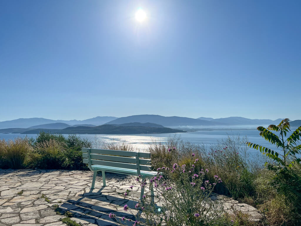 A viewpoint on a promontory near Kalami with a turquoise bench and views out to the Albanian coast. Copyright@2025 NancyRoberts