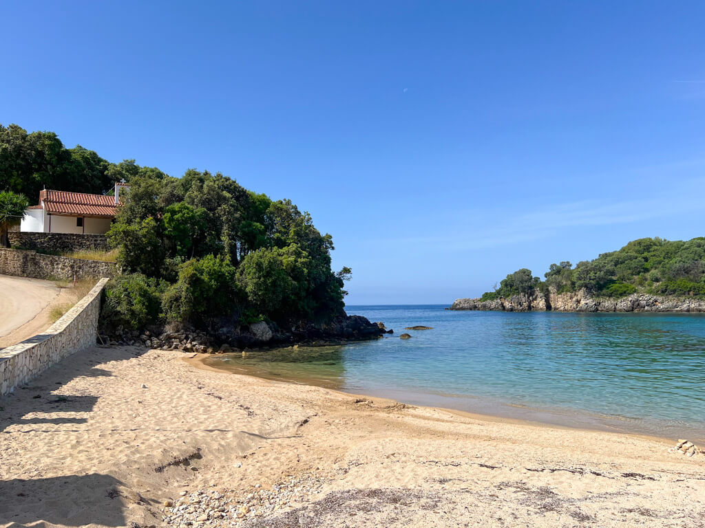 Agia Paraskevi beach near Sivota Greece. A whitewashed chapel overlooks the bay and a wooded islet. Copyright@2025 NancyRoberts