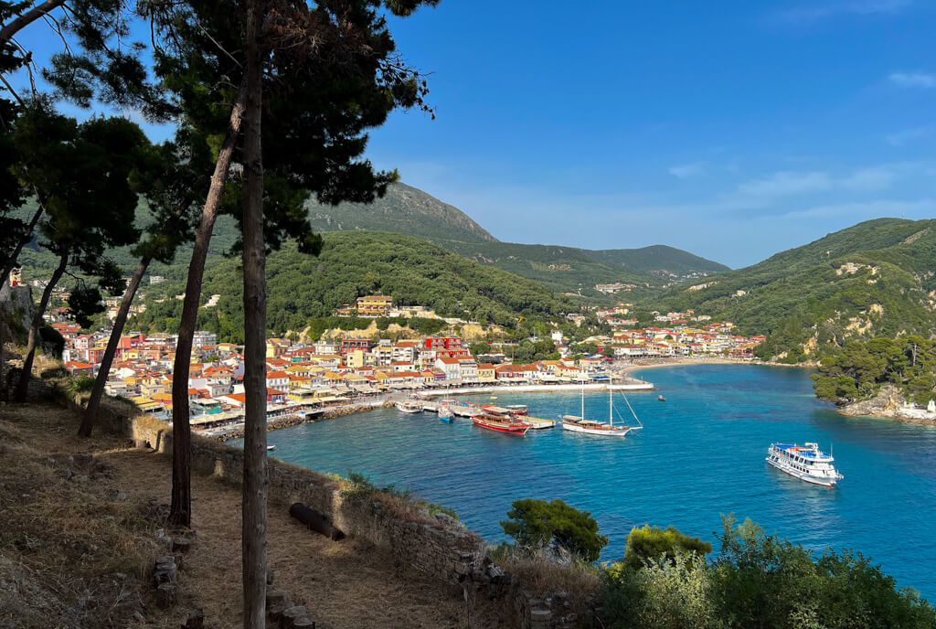 View between Scots pines from Parga castle to the bay and harbour with a ship leaving the port. Copyright@2025 NancyRoberts