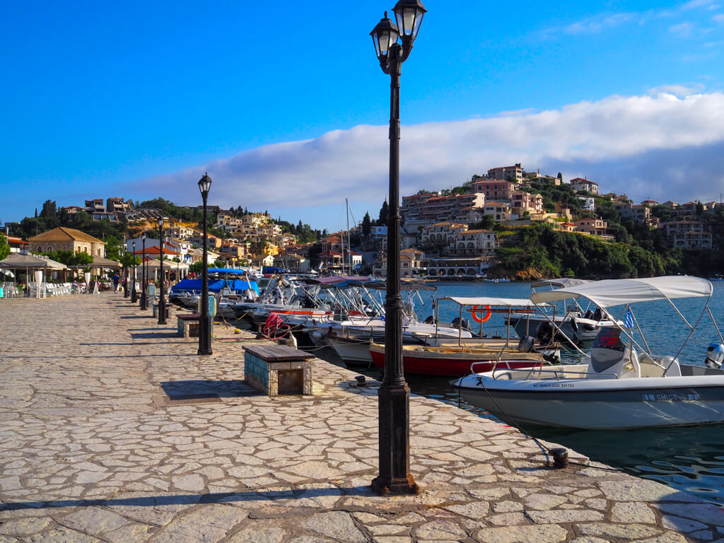 Syvota Greece, view of waterfront promenade with iron lampposts and small boats tied to the quay. Copyright@2025 NancyRoberts