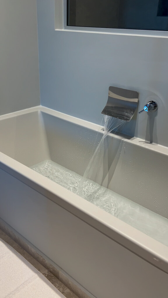 Waterfall tap filling the deep modern bath in the suite. Copyright@2025 NancyRoberts