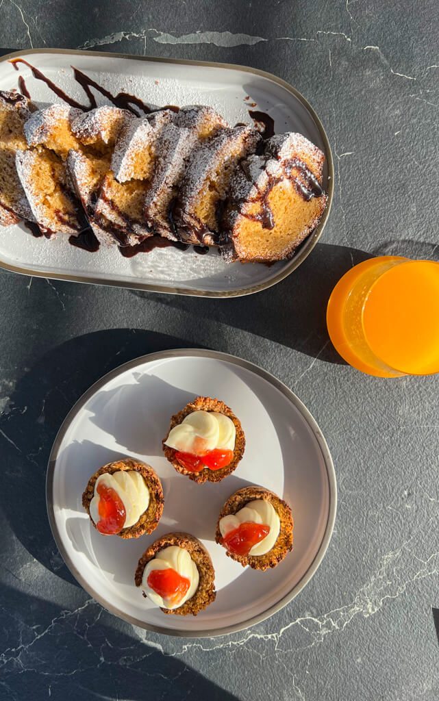 Breakfast dishes including a sliced loaf cake and oat buns with orange juice. Copyright@2025 NancyRoberts