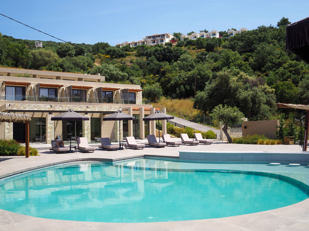 Exterior of Arete Lifestyle Hotel in Sivota, Greece, showing oval pool and quiet wooded hillside beside the hotel. Copyright@2025 NancyRoberts