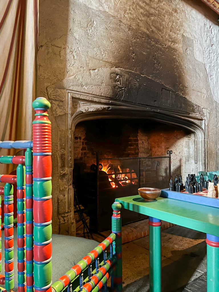 Bright green and red striped chair inspired by medieval original, pulled up to the fireplace in Dover Castle. Copyright@2025 Nancy Roberts