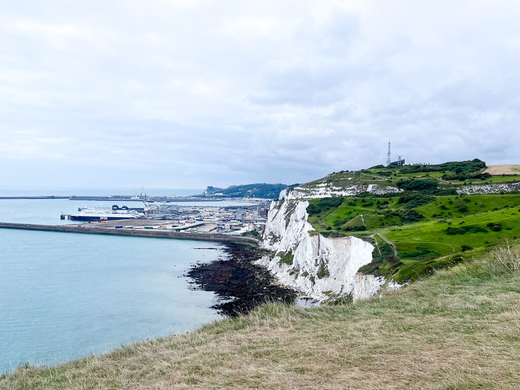 View from White Cliffs coast path towards the chalk white cliffs topped with grass and Dover port in the background. Copyright@2025 Nancy Roberts